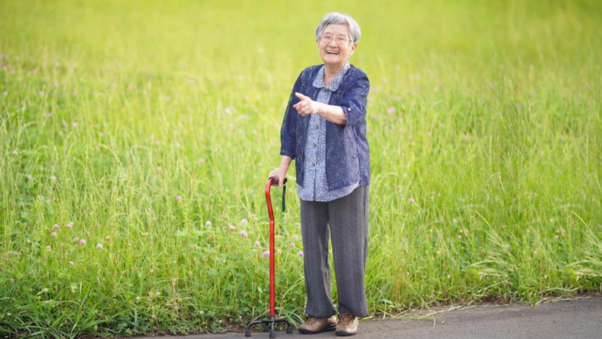 草花の咲く道で、杖を持って笑顔で散歩する高齢女性