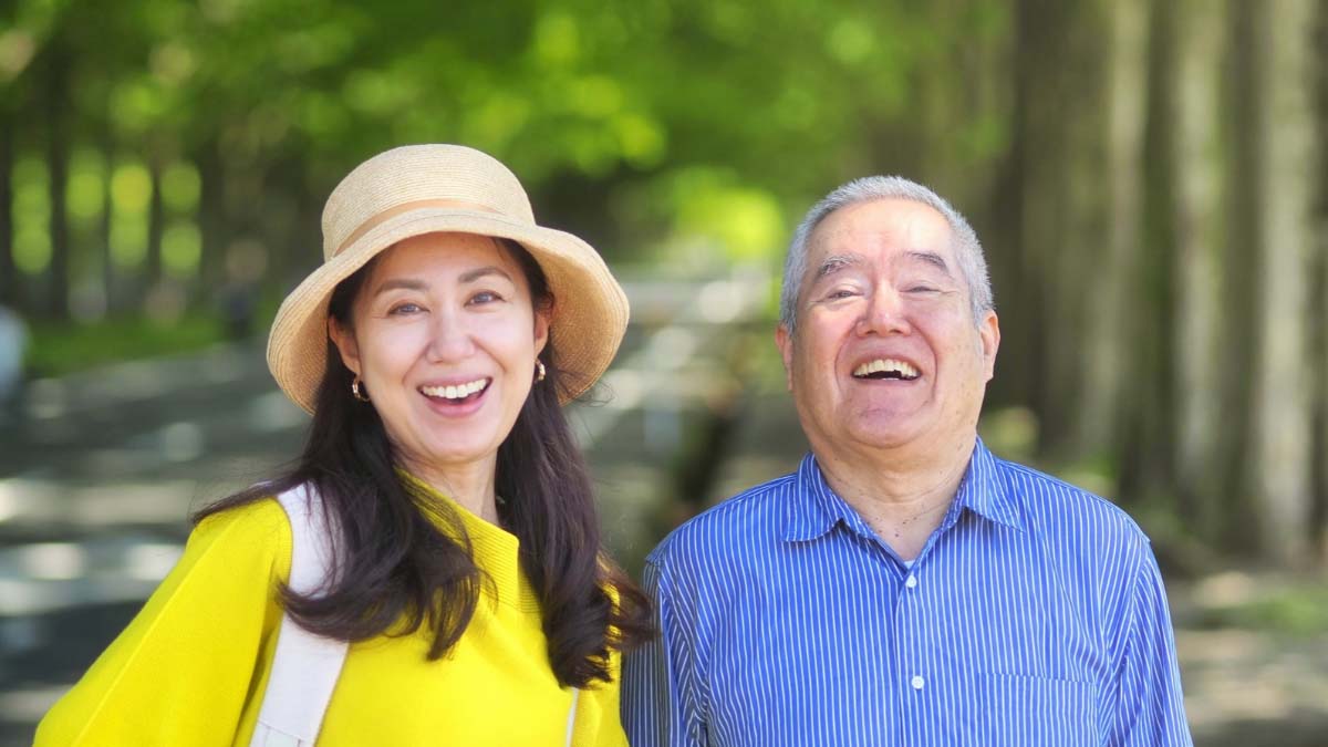 並木道で一緒に散歩し、笑顔を見せる高齢男性と付き添いの女性